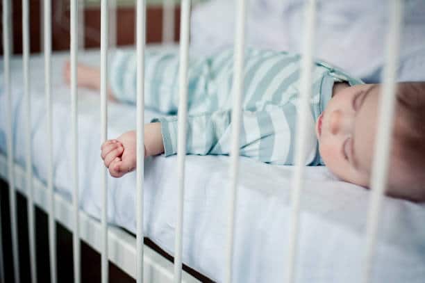 Bébé qui dort paisiblement dans son lit à barreaux