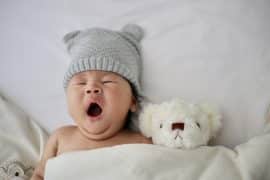 Bébé qui baille couché dans son lit avec sa peluche pour faire la sieste