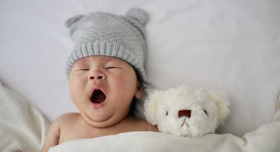 Bébé qui baille couché dans son lit avec sa peluche pour faire la sieste