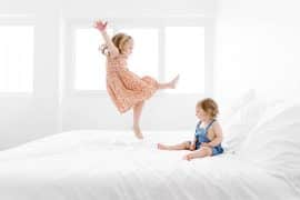 Deux enfants qui sautent sur un lit dans une pièce blanche lumineuse