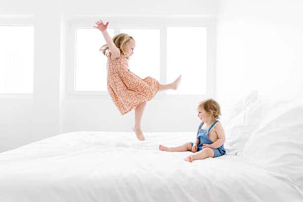 Deux enfants qui sautent sur un lit dans une pièce blanche lumineuse